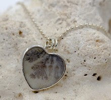 Heart shaped dendritic agate set in sterling silver and resting on a piece of fossilized coral.